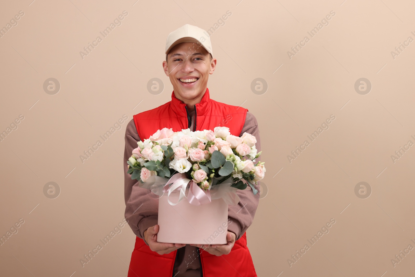 Photo of Smiling delivery man giving gift box with beautiful floral composition on beige background