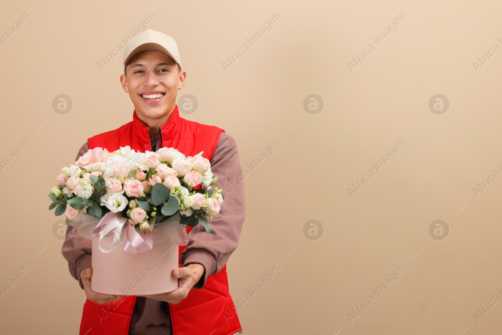 Photo of Smiling delivery man giving gift box with beautiful floral composition on beige background. Space for text