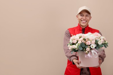 Photo of Smiling delivery man giving gift box with beautiful floral composition on beige background. Space for text