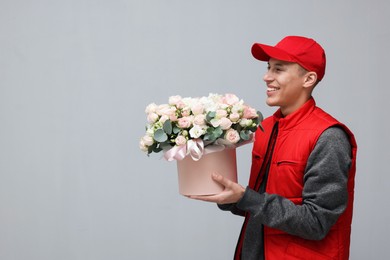 Photo of Smiling delivery man holding gift box with beautiful floral composition on grey background. Space for text