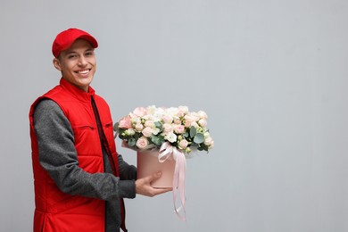 Smiling delivery man holding gift box with beautiful floral composition on grey background. Space for text