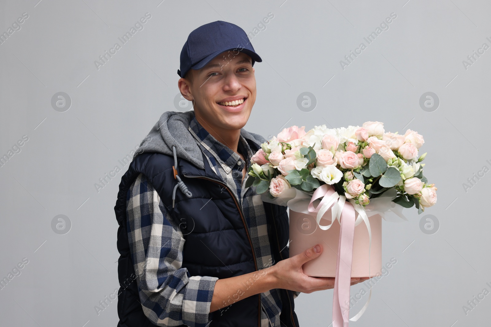 Photo of Smiling delivery man holding gift box with beautiful floral composition on grey background