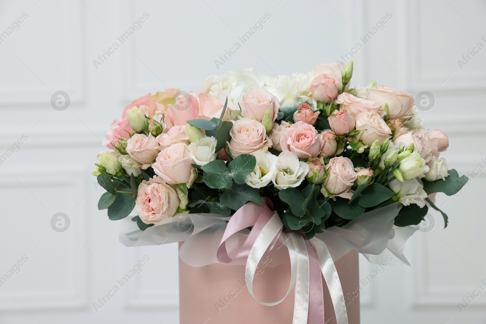 Photo of Gift box with bouquet of beautiful flowers and eucalyptus branches against blurred background, closeup