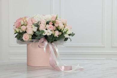 Photo of Gift box with bouquet of beautiful flowers and eucalyptus branches on marble table against white wall. Space for text