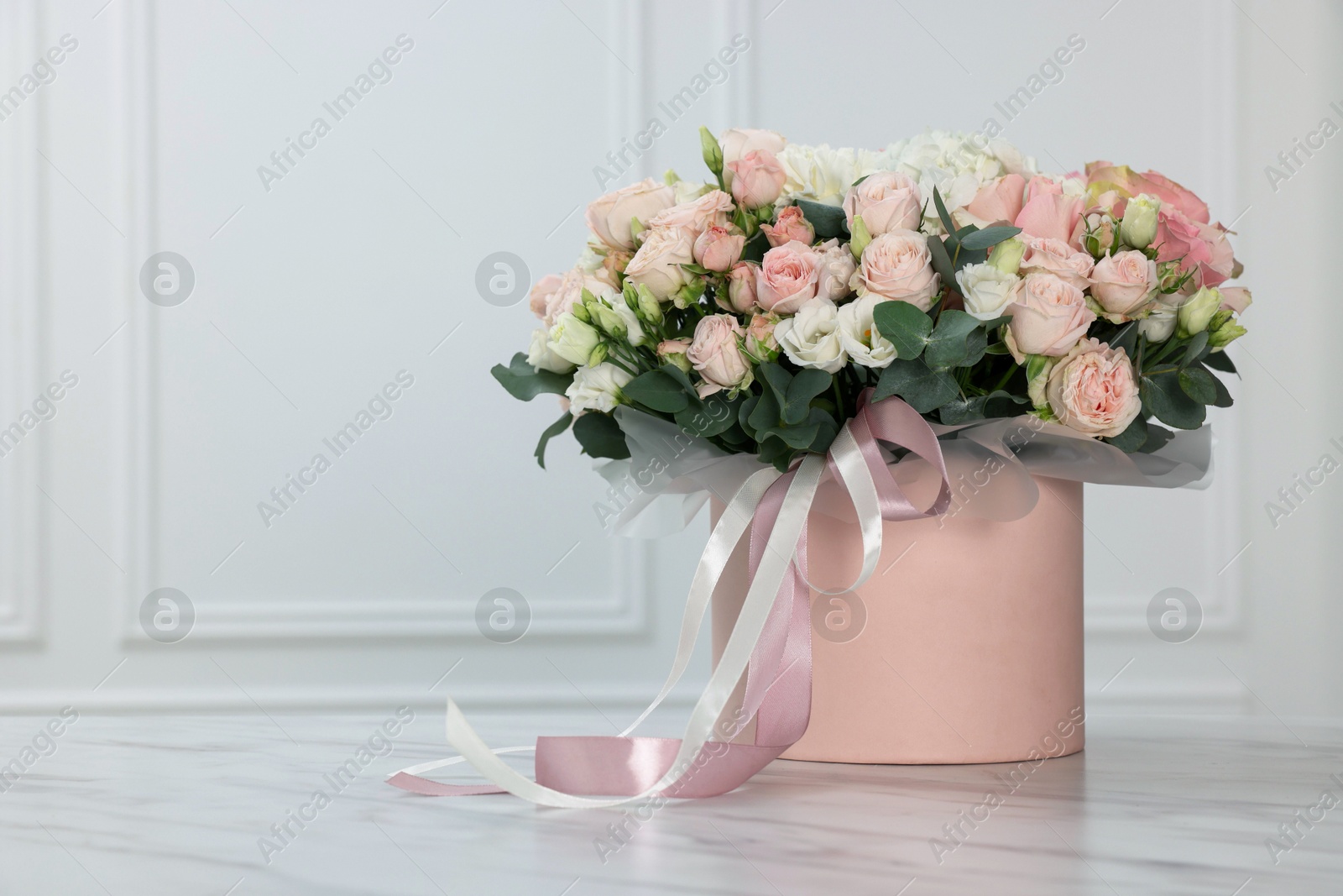 Photo of Gift box with bouquet of beautiful flowers and eucalyptus branches on marble table against white wall. Space for text