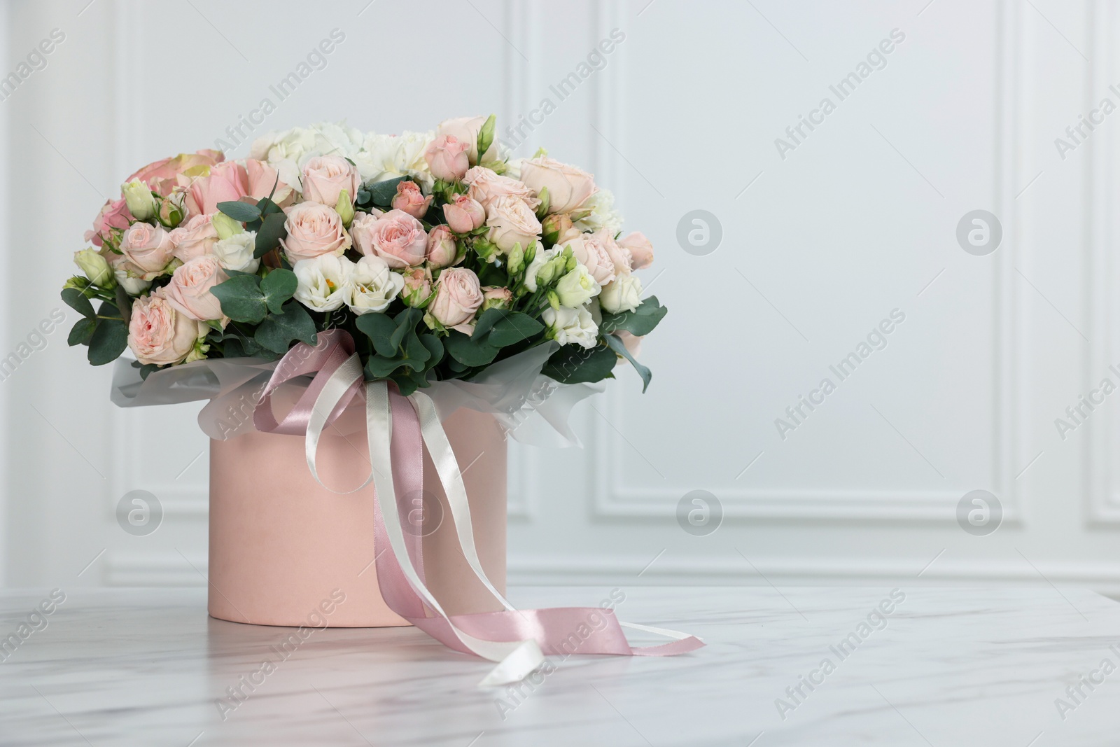 Photo of Gift box with bouquet of beautiful flowers and eucalyptus branches on marble table against white wall. Space for text