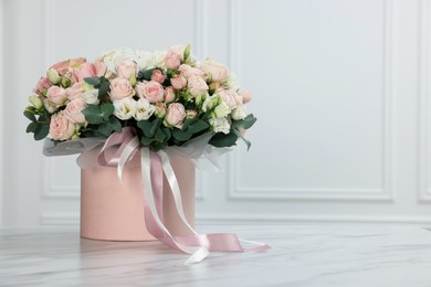 Photo of Gift box with bouquet of beautiful flowers and eucalyptus branches on marble table against white wall. Space for text