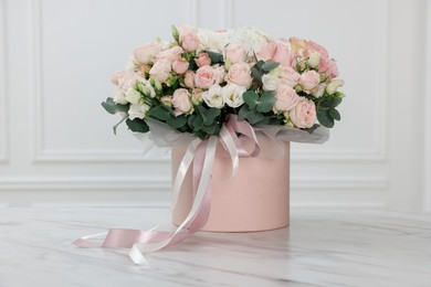 Photo of Gift box with bouquet of beautiful flowers and eucalyptus branches on marble table against white wall