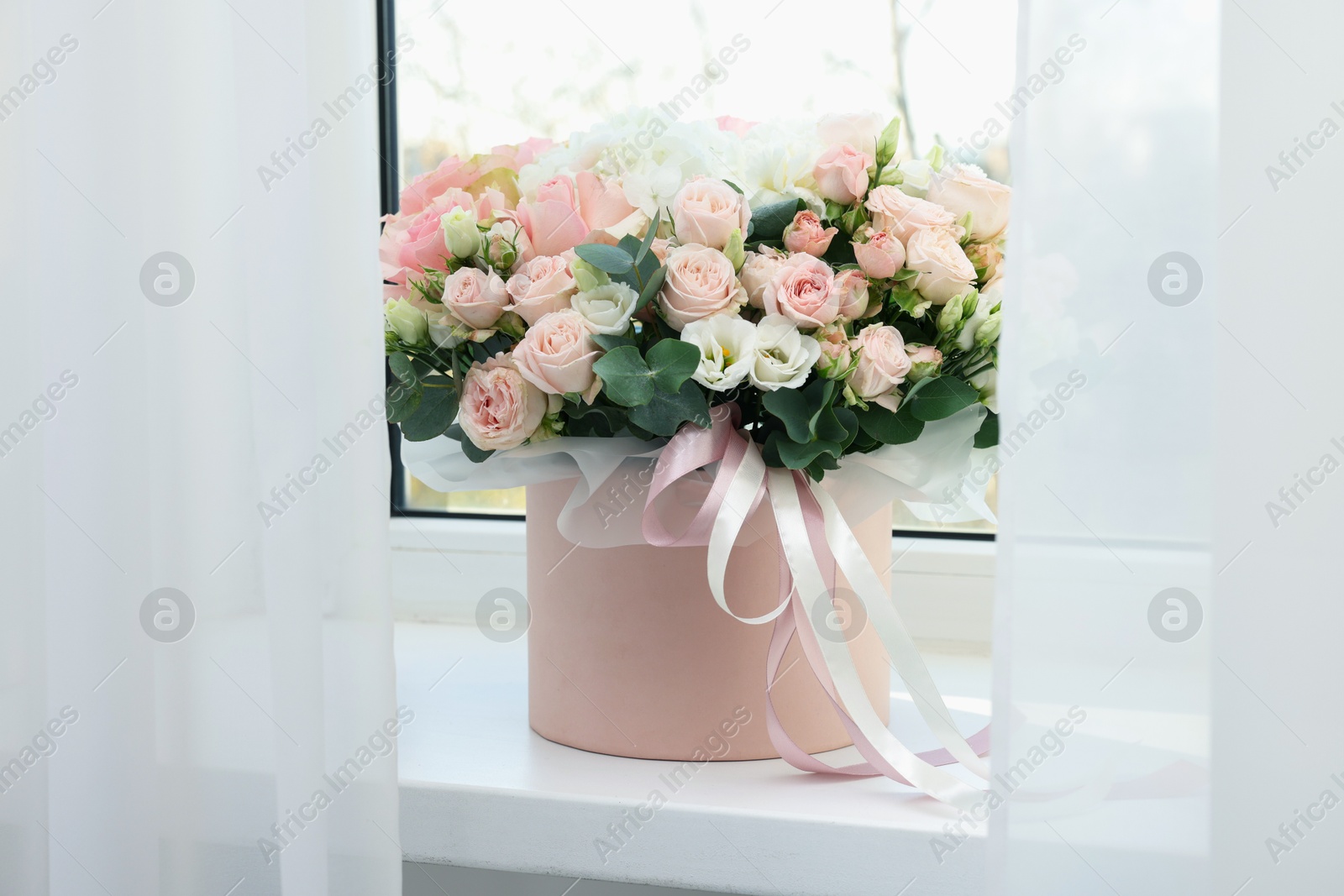 Photo of Gift box with bouquet of beautiful flowers and eucalyptus branches on window sill