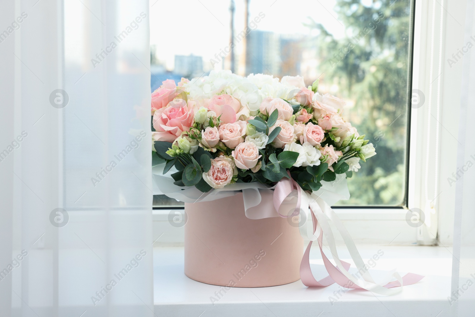 Photo of Gift box with bouquet of beautiful flowers and eucalyptus branches on window sill