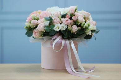 Photo of Gift box with bouquet of beautiful flowers and eucalyptus branches on wooden table against light blue wall