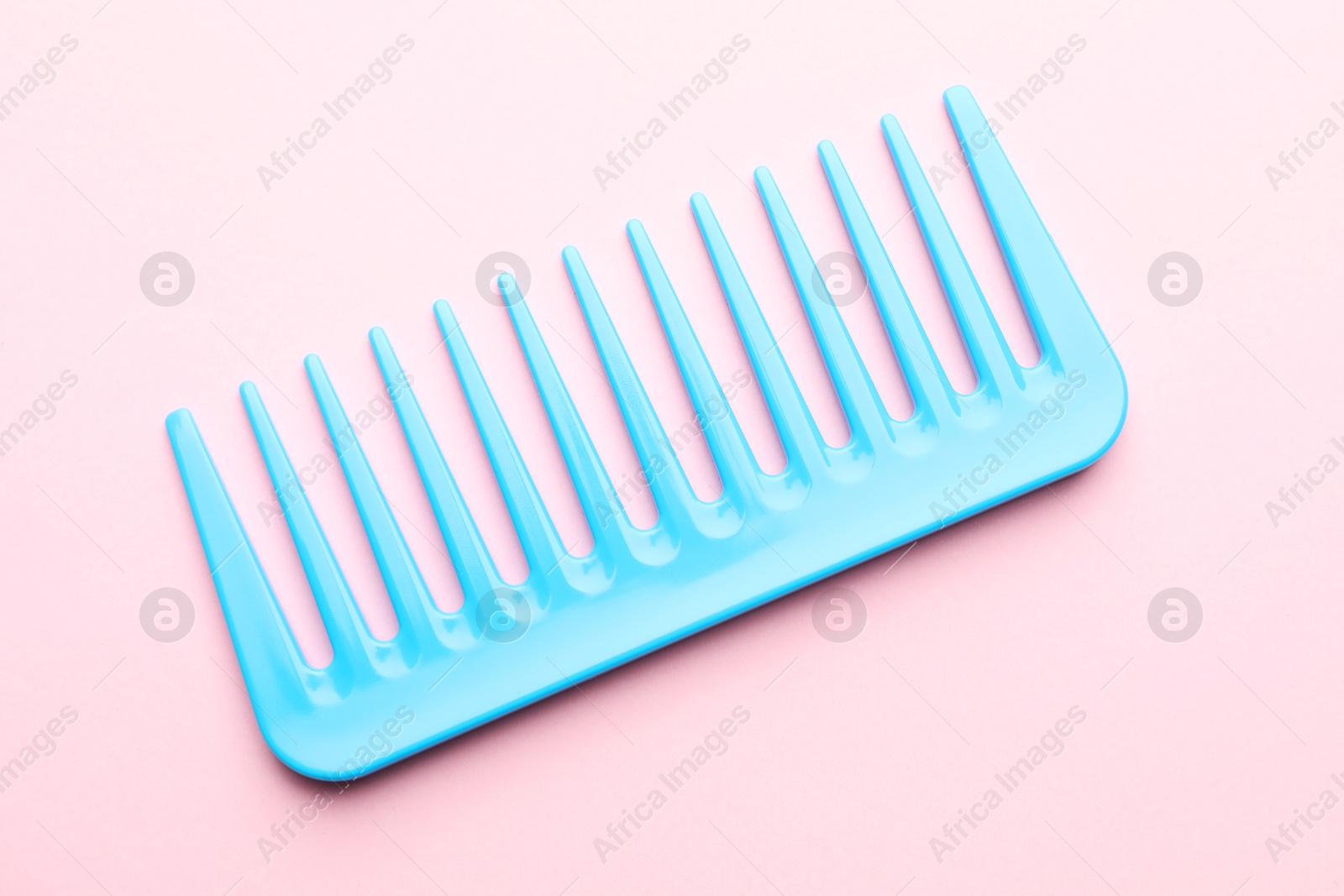 Photo of One light blue plastic comb on pink background, top view