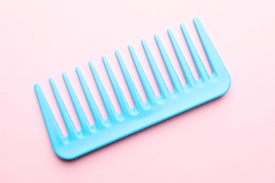 Photo of One light blue plastic comb on pink background, top view