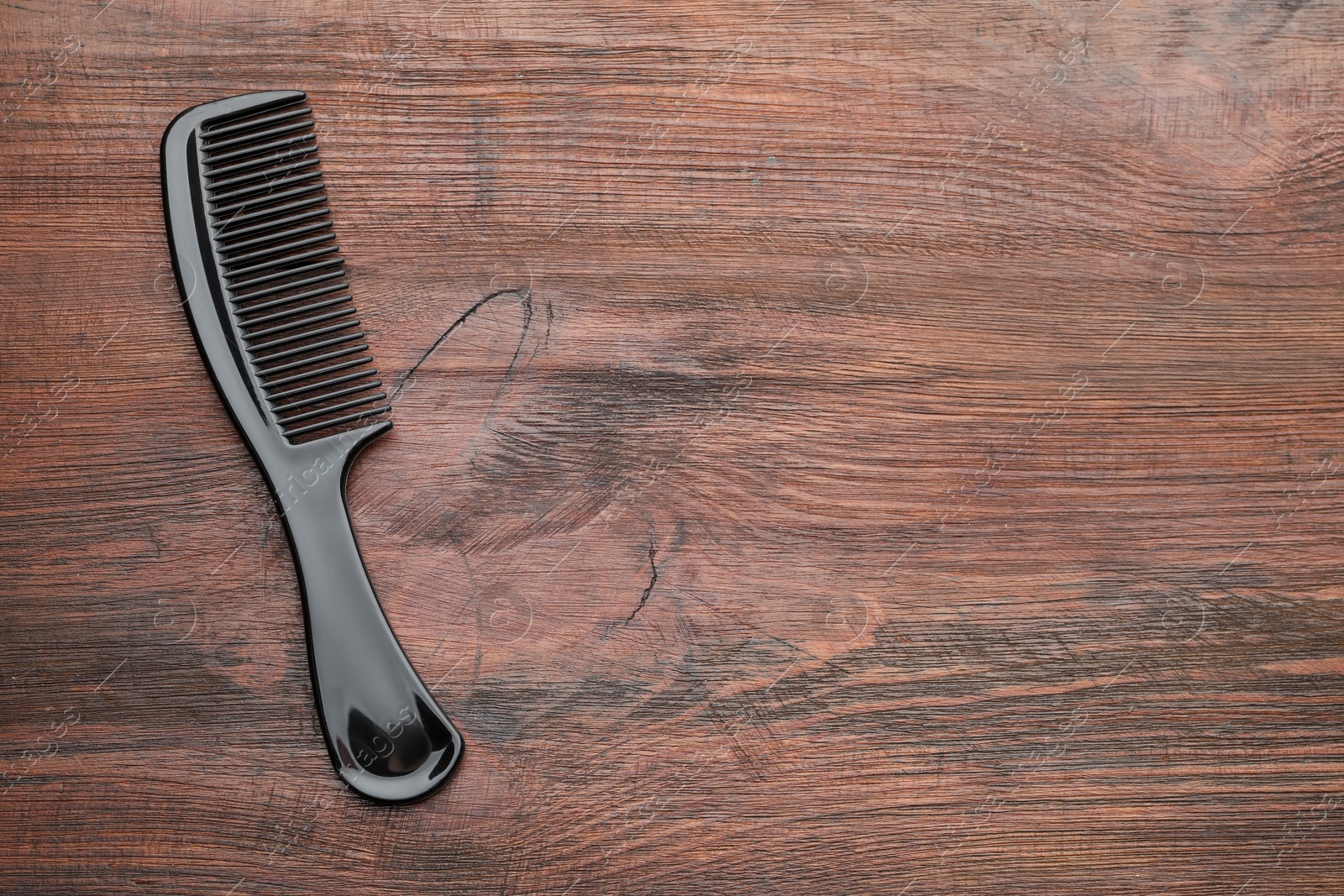 Photo of One black plastic comb on wooden background, top view. Space for text