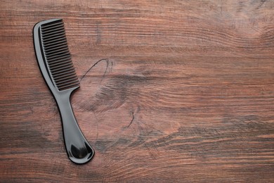 Photo of One black plastic comb on wooden background, top view. Space for text