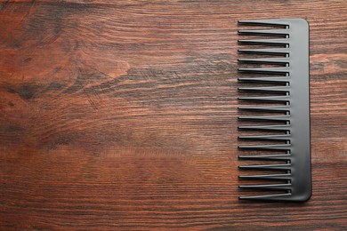 Photo of One black plastic comb on wooden background, top view. Space for text