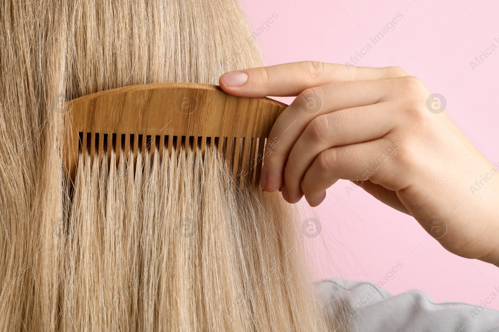 Photo of Woman brushing hair with wooden comb on pink background, closeup