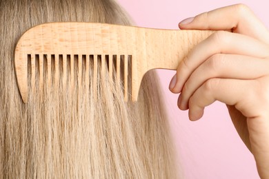 Photo of Woman brushing hair with wooden comb on pink background, closeup