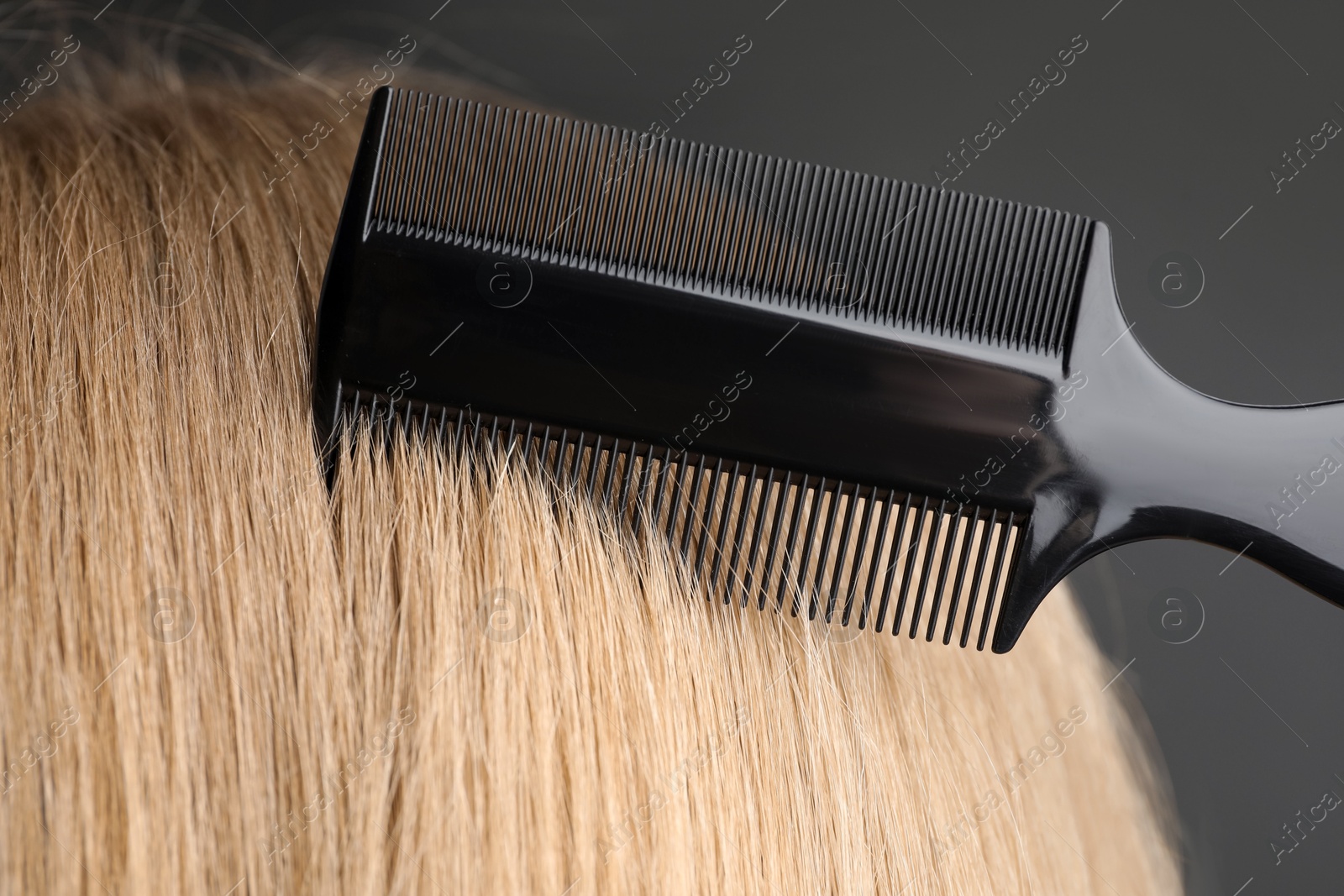 Photo of Woman brushing hair with plastic comb on grey background, closeup