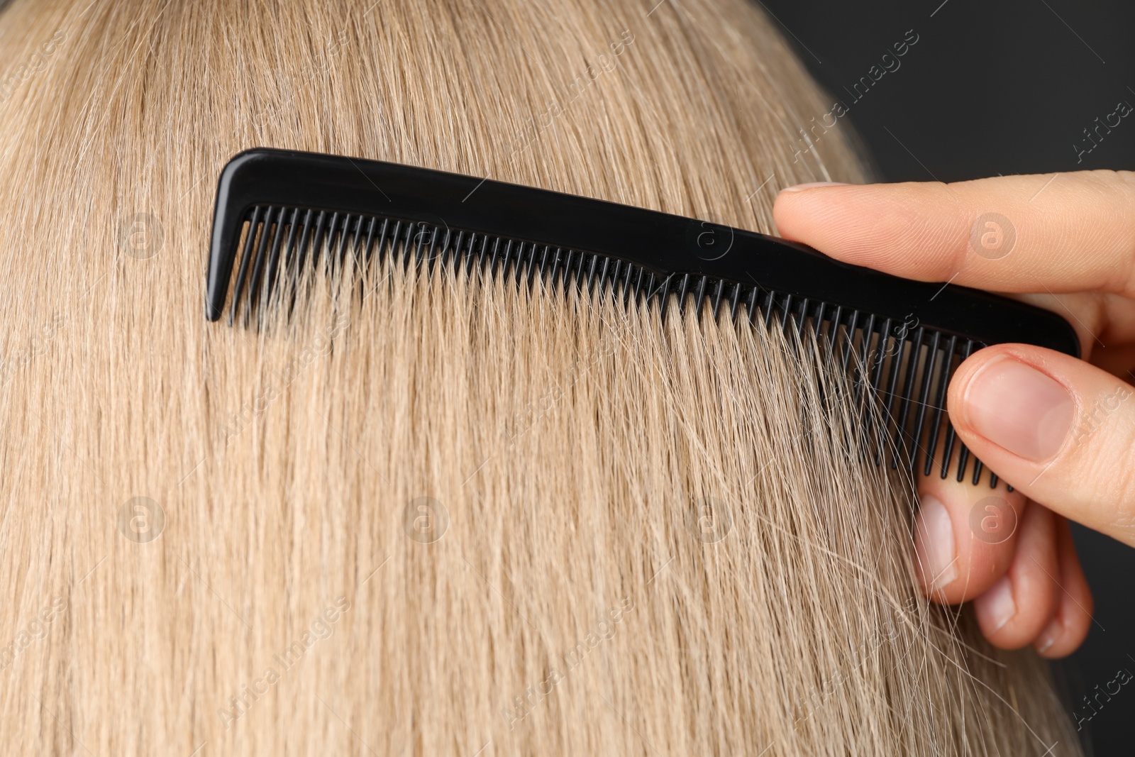 Photo of Woman brushing hair with plastic comb on dark background, closeup