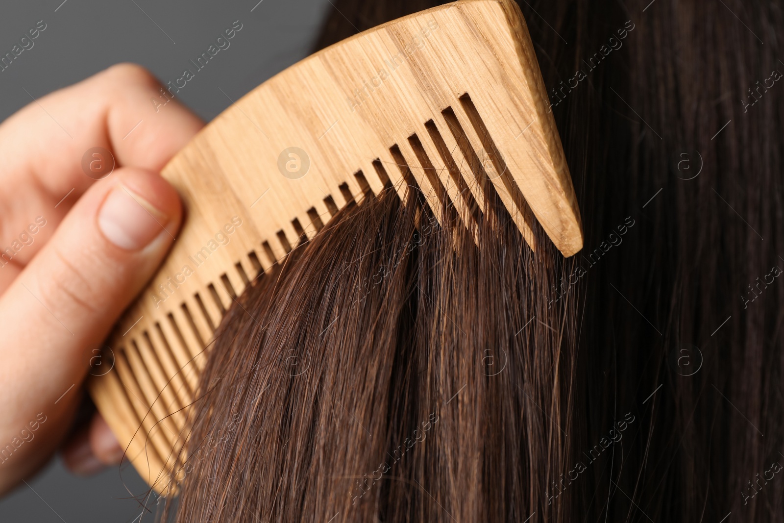 Photo of Woman brushing hair with wooden comb on grey background, closeup