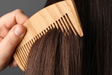 Photo of Woman brushing hair with wooden comb on grey background, closeup