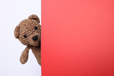 Photo of Cute knitted bear peeking out from red card on white background, space for text