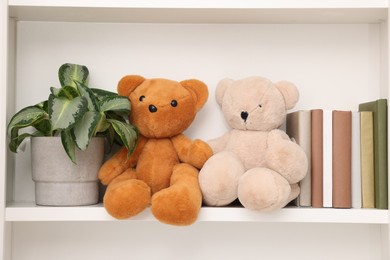 Photo of Cute teddy bears, books and houseplant on shelf indoors