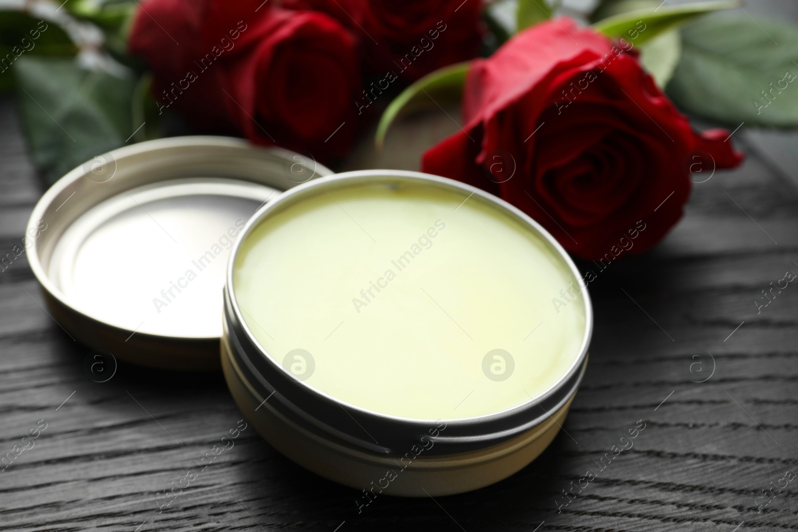 Photo of Natural solid perfume and roses on black wooden table, closeup