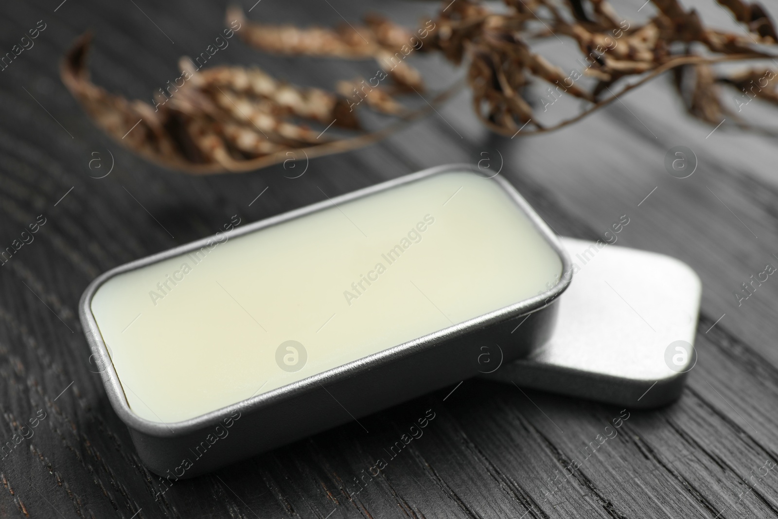 Photo of Natural solid perfume and dry branch on black wooden table, closeup