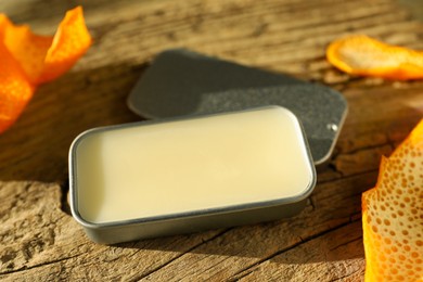 Photo of Natural solid perfume in container and orange peels on wooden table, closeup