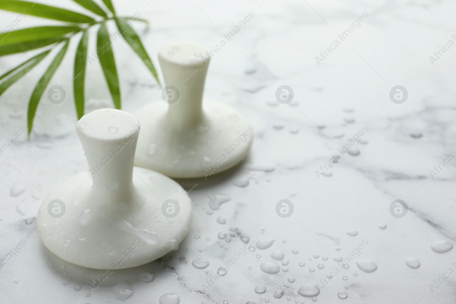 Photo of Wet spa stones and green palm leaf on white marble table, closeup. Space for text