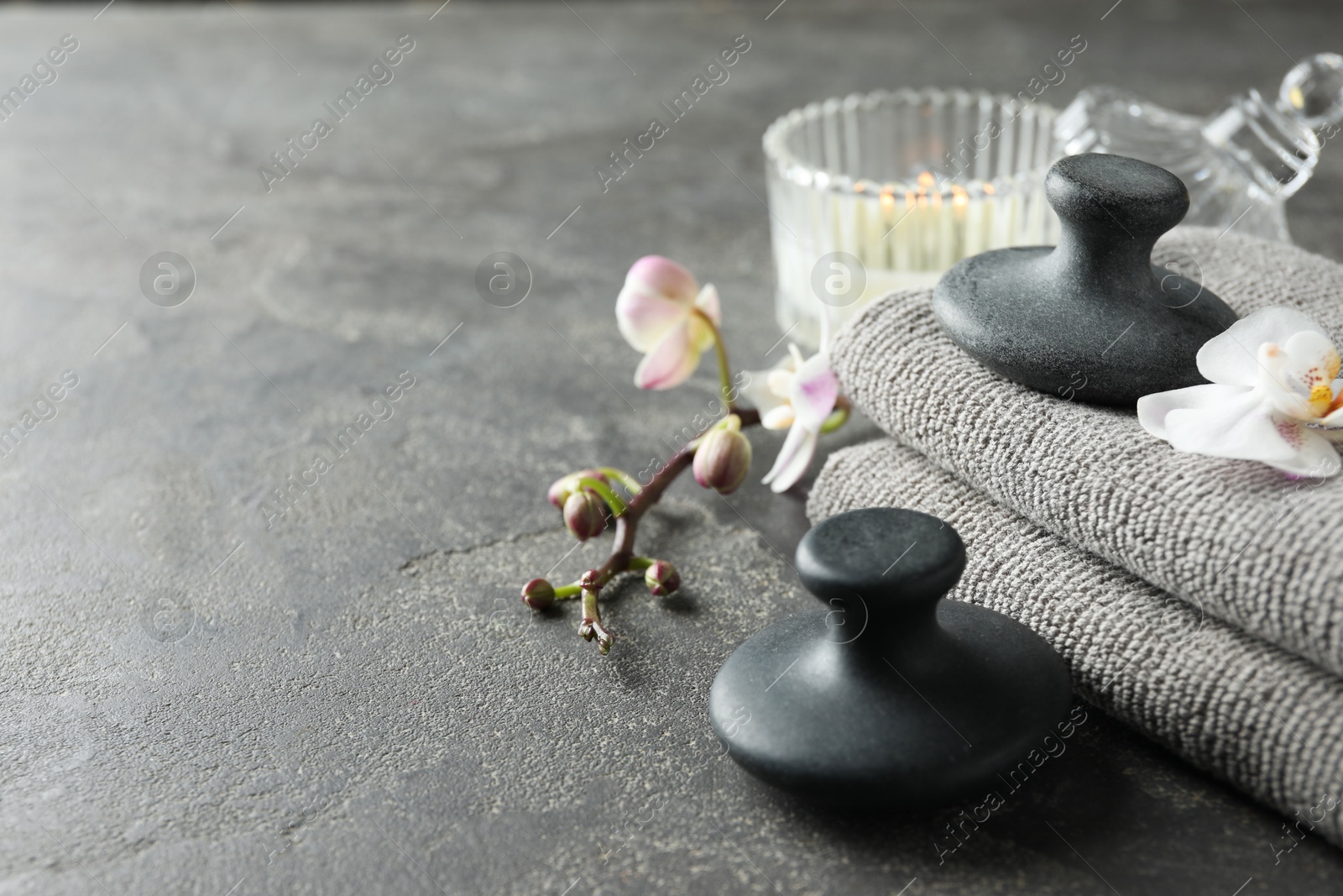 Photo of Spa stones, towels, orchid flowers and candle on grey table, closeup. Space for text