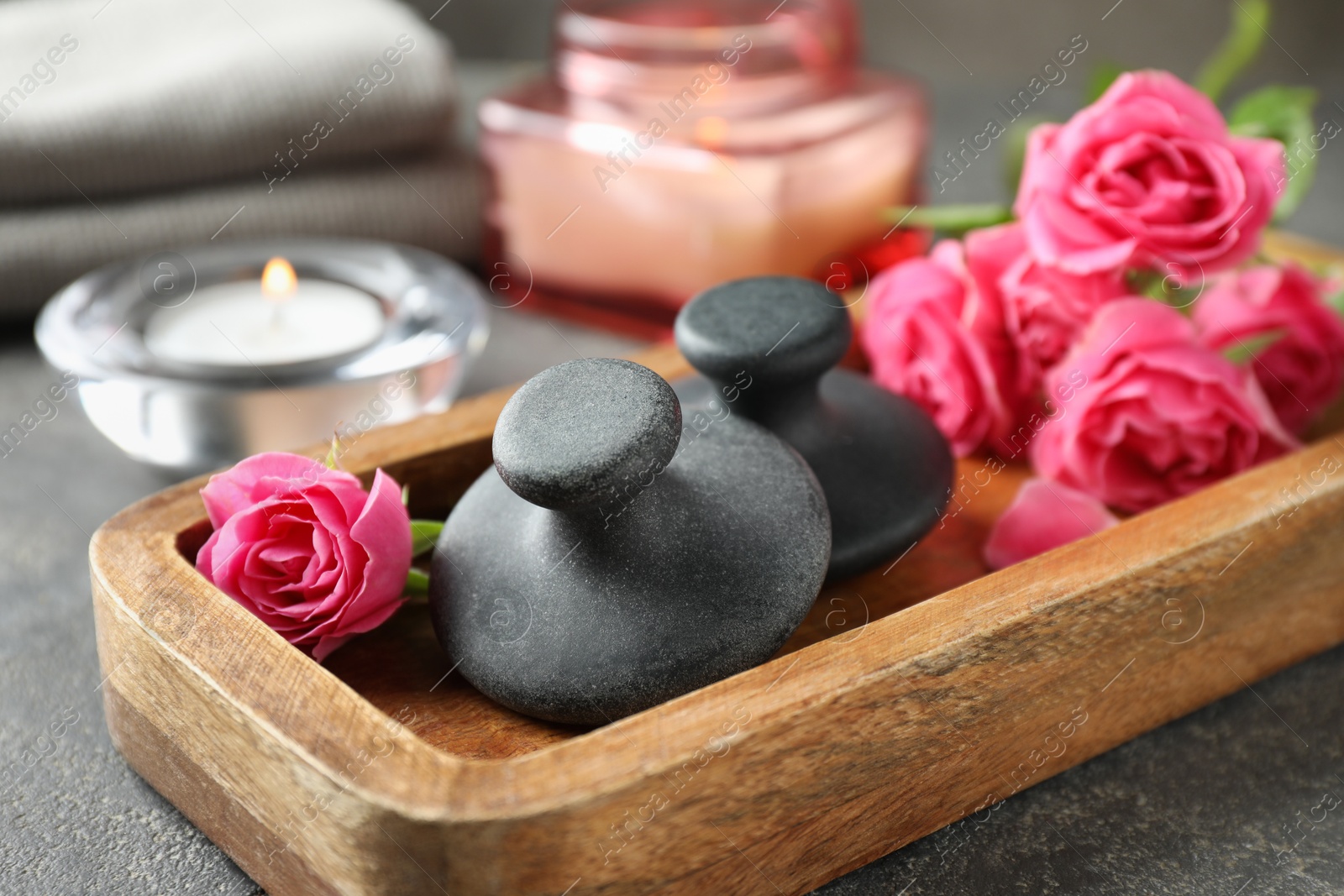 Photo of Spa stones, rose flowers and candles on grey table, closeup