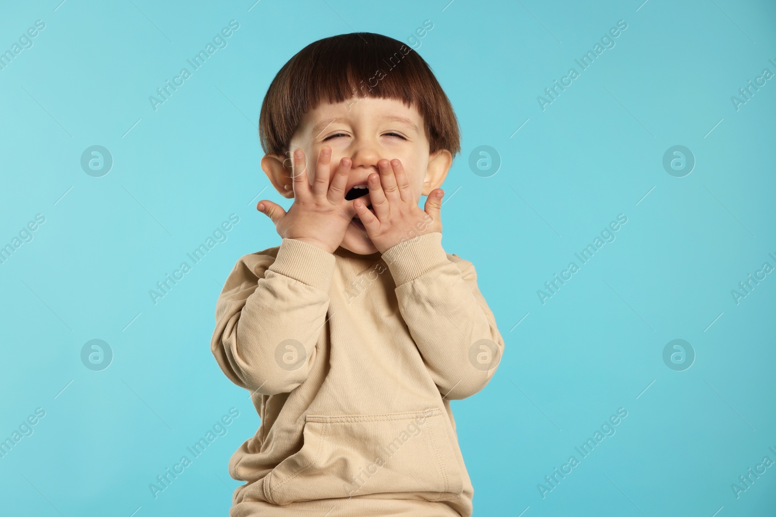 Photo of Portrait of emotional little boy covering mouth on light blue background