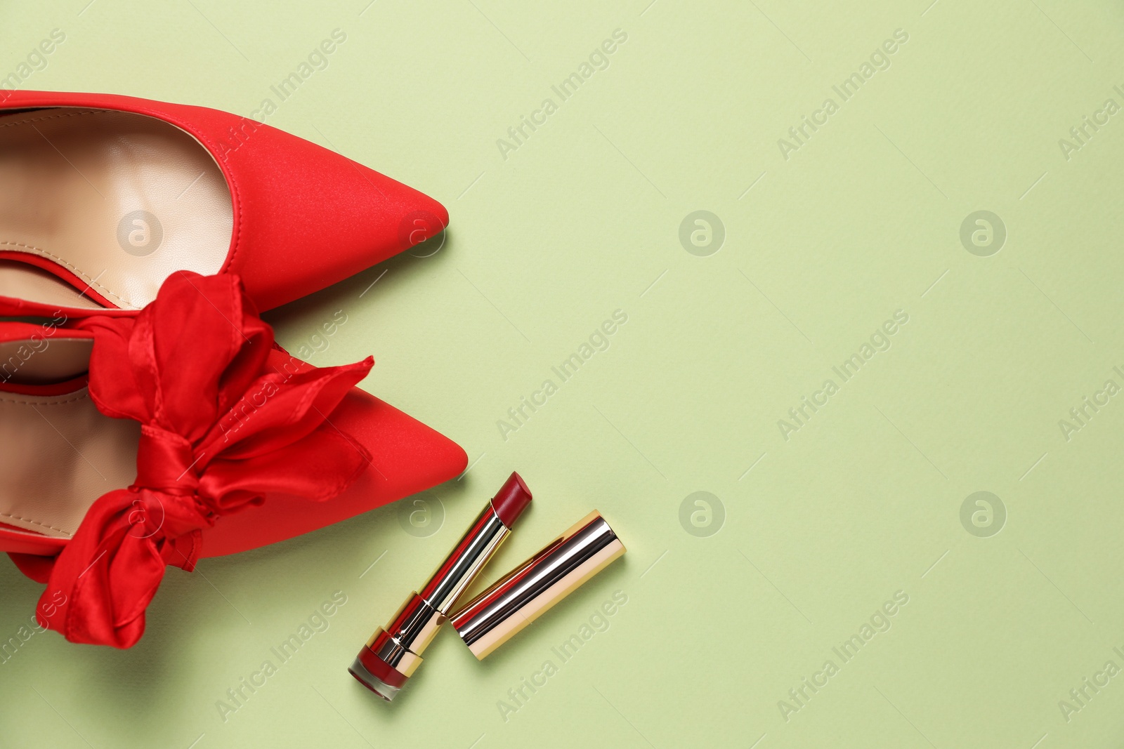 Photo of Stylish red women's shoes and lipstick on light green background, flat lay. Space for text