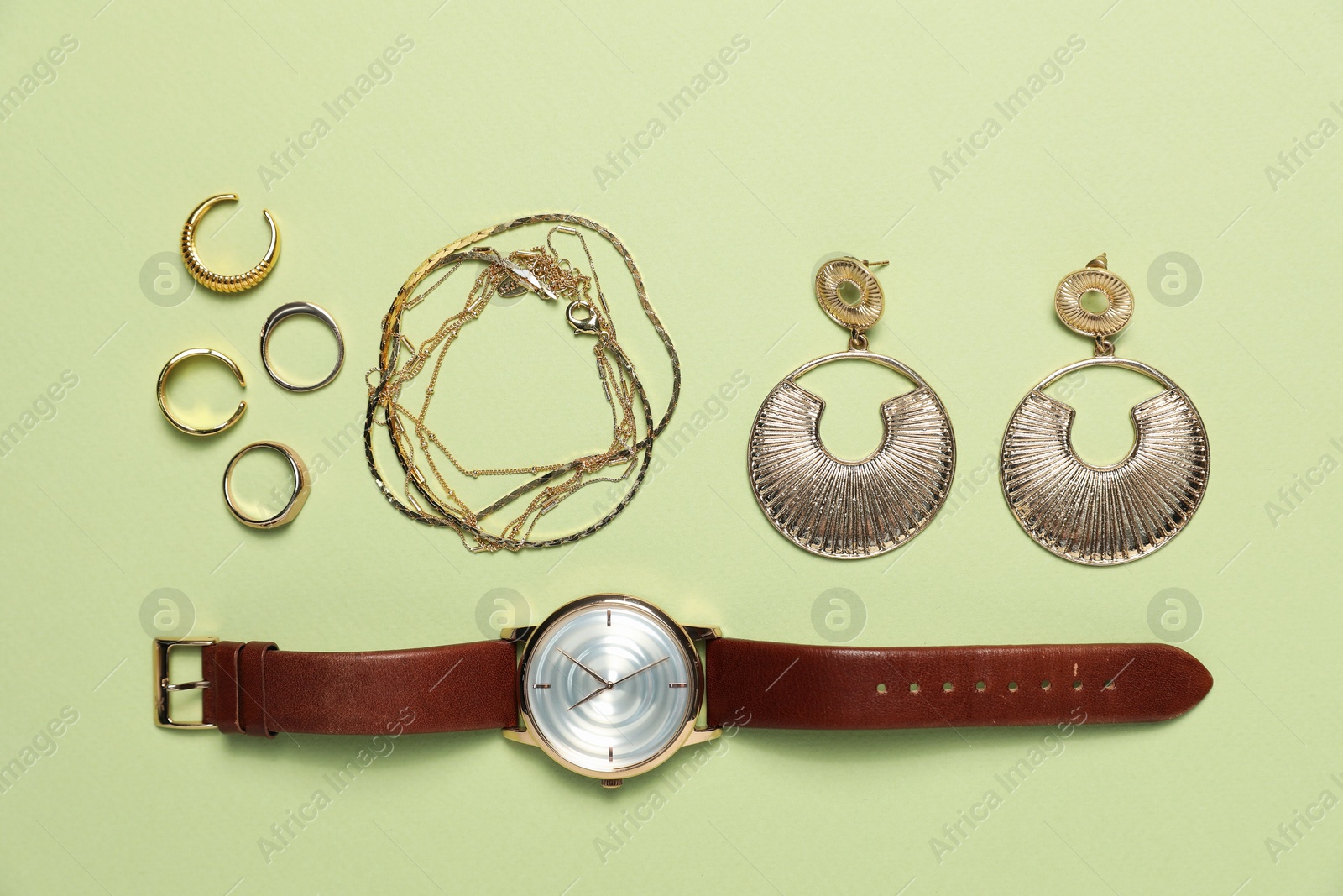 Photo of Flat lay composition with golden jewelry and watch on light green background