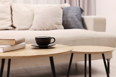 Photo of Nesting tables with cup of drink and books near sofa at home