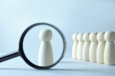 Photo of Human resources concept. Looking at wooden figure through magnifying glass on light background, closeup