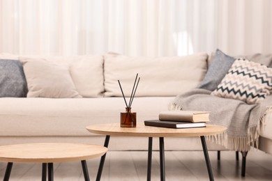 Photo of Nesting tables with books and reed diffuser near sofa at home