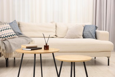 Photo of Nesting tables with books and reed diffuser near sofa at home