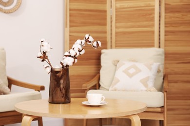 Photo of Coffee table with cotton flowers and cup of drink near armchairs at home