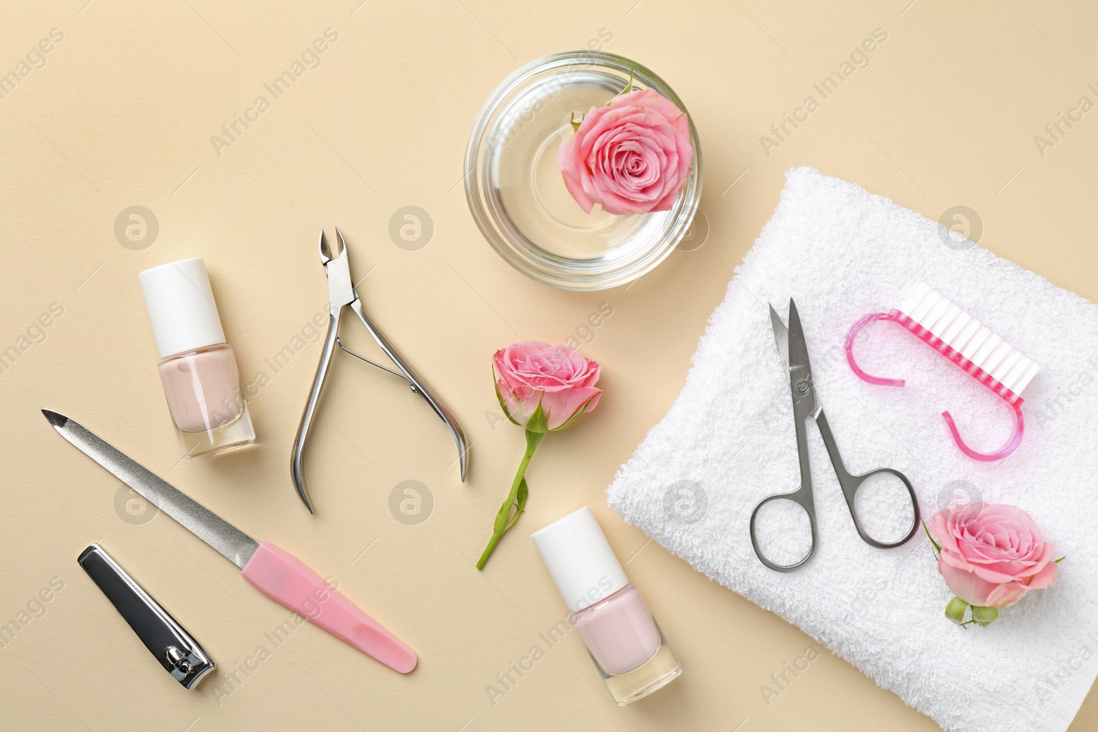 Photo of Set of pedicure tools and flowers on beige background, flat lay