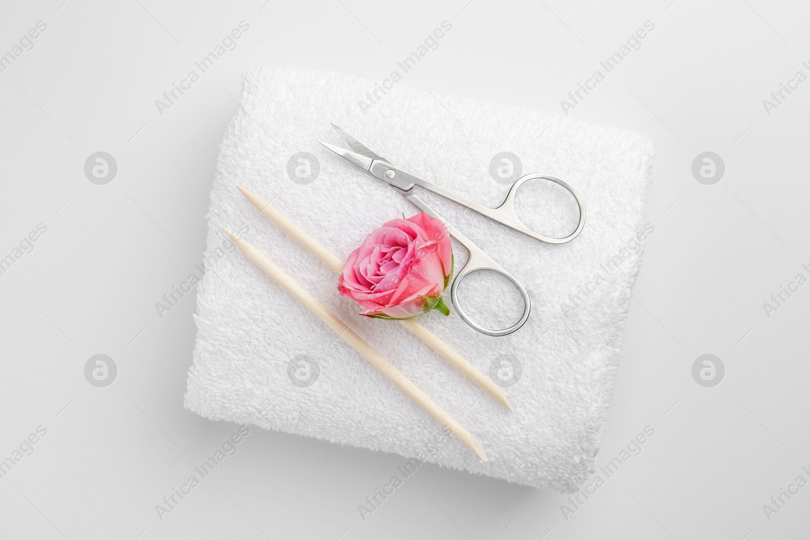 Photo of Pedicure procedure. Towel with scissors, orange sticks and flower on light background, top view