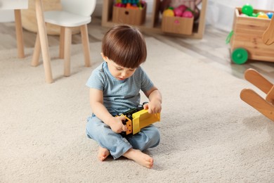 Photo of Cute little boy playing with toy truck on floor at home