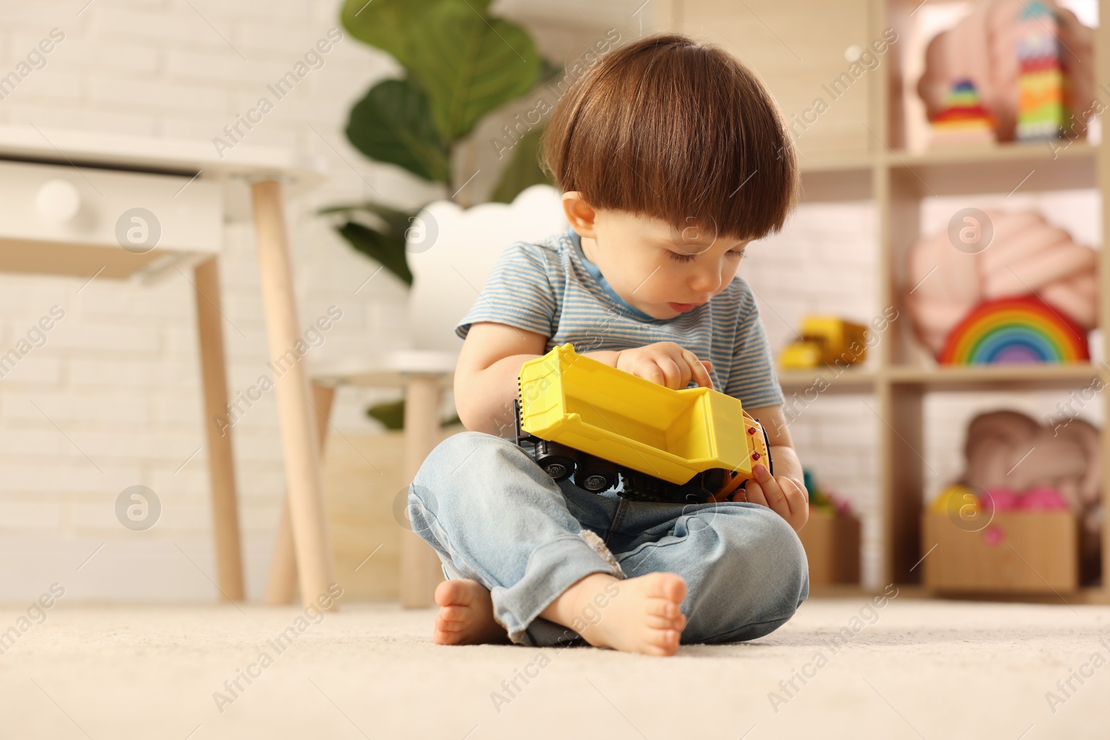 Photo of Cute little boy playing with toy truck on floor at home