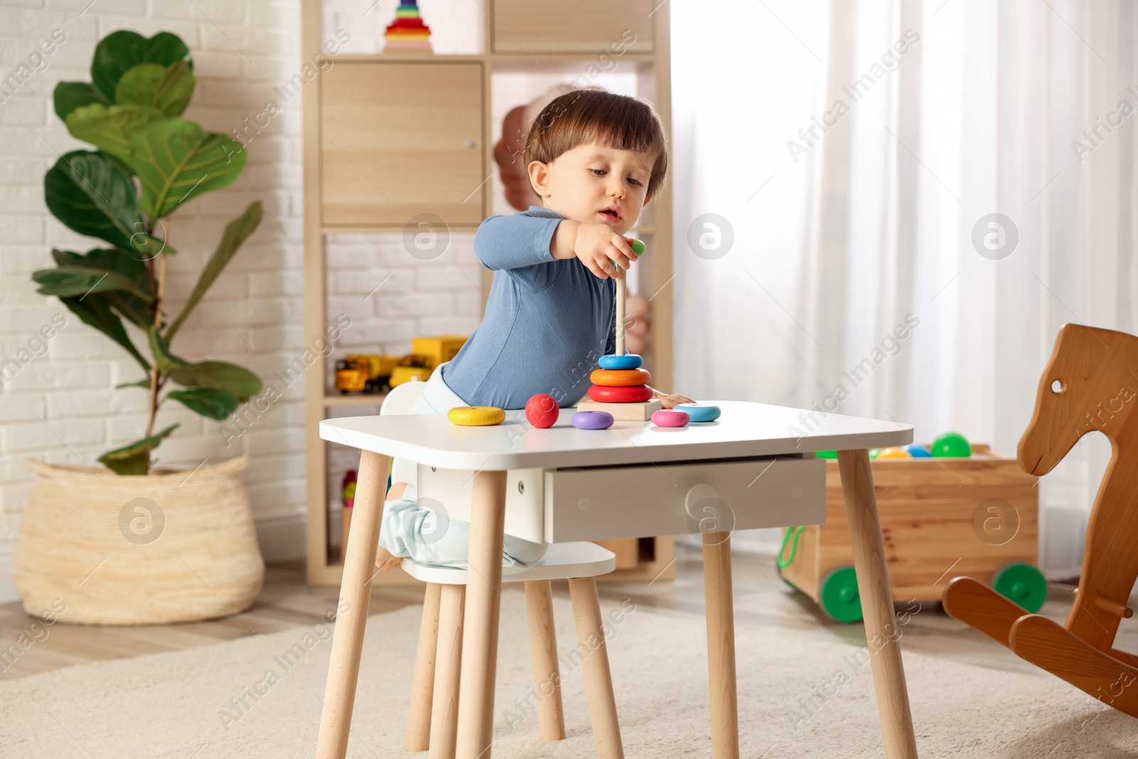 Photo of Cute little boy playing with toy pyramid at table indoors