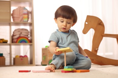 Photo of Cute little boy playing with toy pyramid on floor at home, space for text