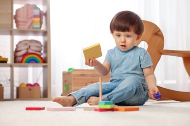 Photo of Cute little boy playing with toy pyramid on floor at home, space for text