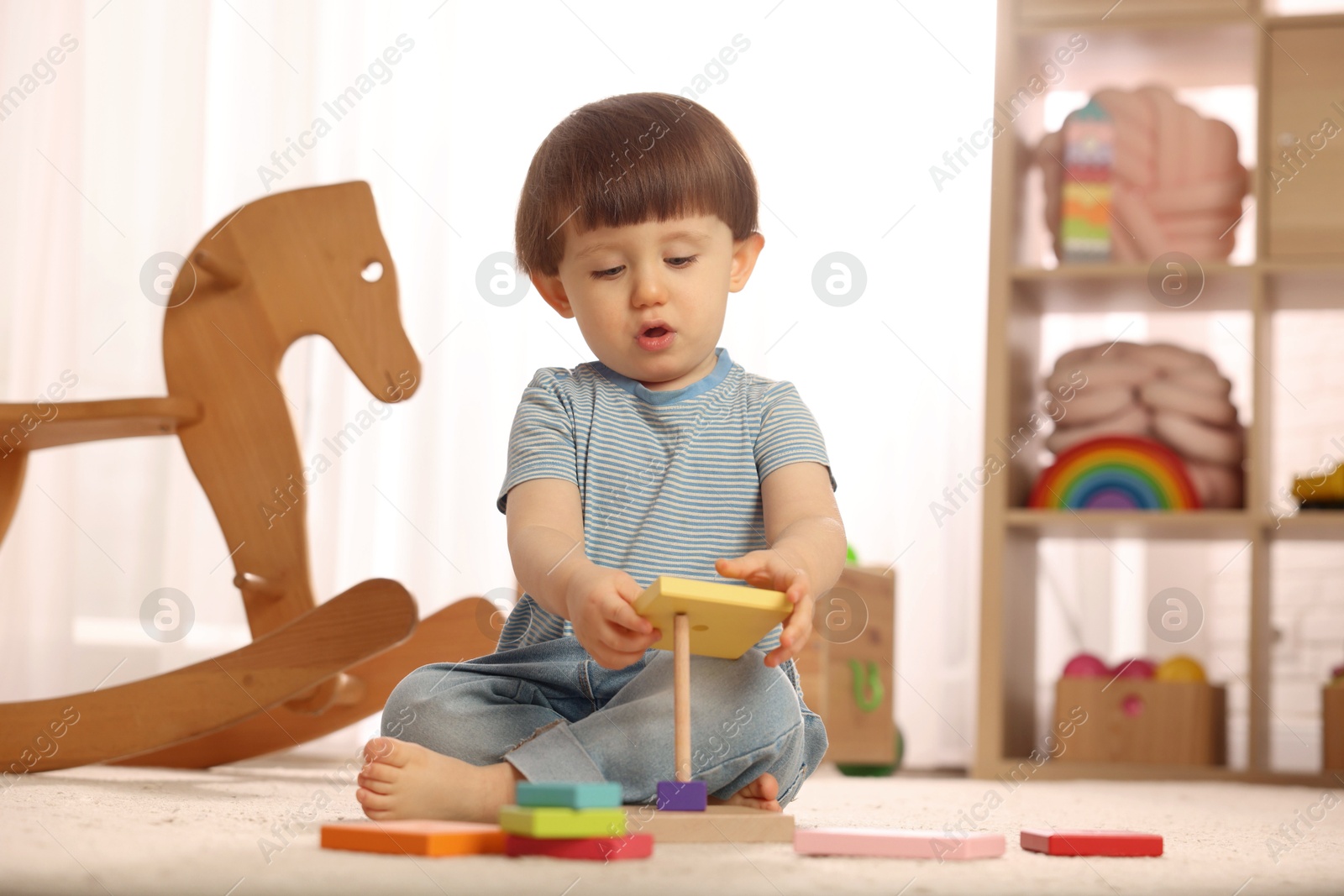 Photo of Cute little boy playing with toy pyramid on floor at home